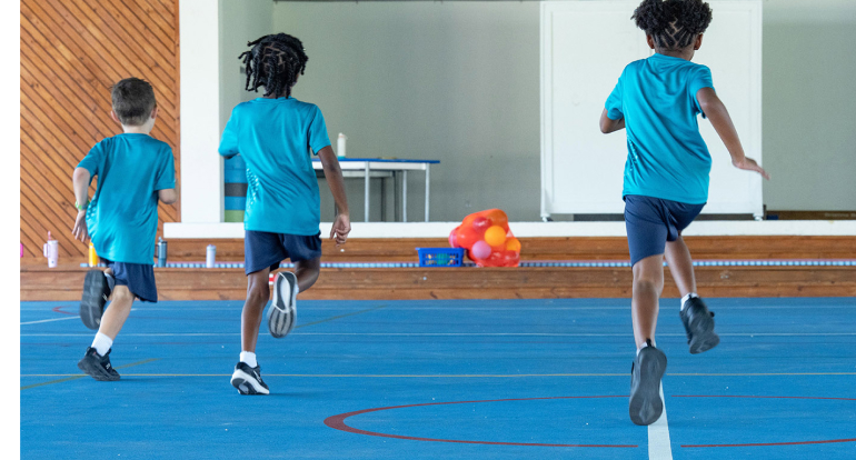 Students running inside a school gym during an after-school club activity.