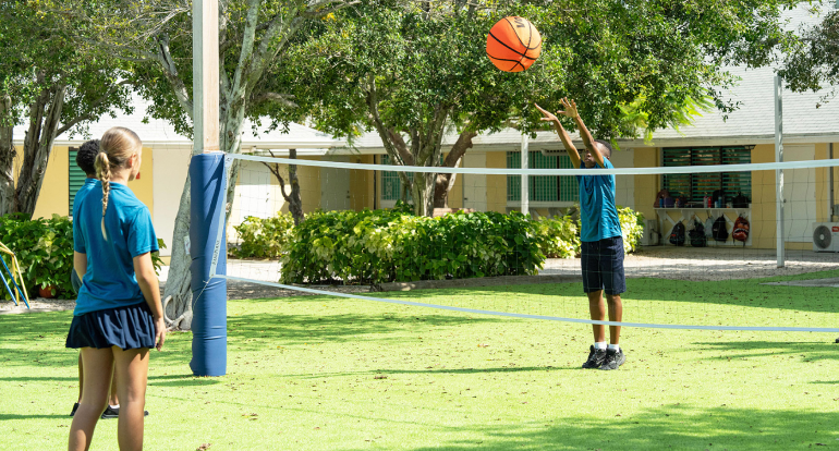 Students playing volleyball outdoors on the school campus sports court.
